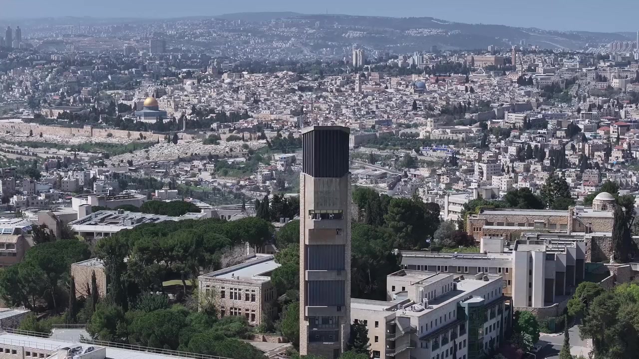 Arka planda genişleyen Kudüs şehir manzarası ve Eski Şehir simgeleriyle Scopus Dağı kampüsünün çan kulesini gösteren yüksek açılı hava çekimi.