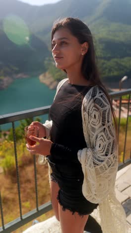 woman enjoying a drink with a view of a lake and mountains