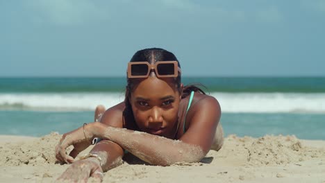 young black girl lays in white sand with ocean waves and blue skies in the background