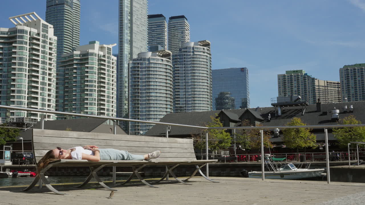 한 여성이 토론토에서 새와 함께 벤치에서 잠을 자고 있습니다.