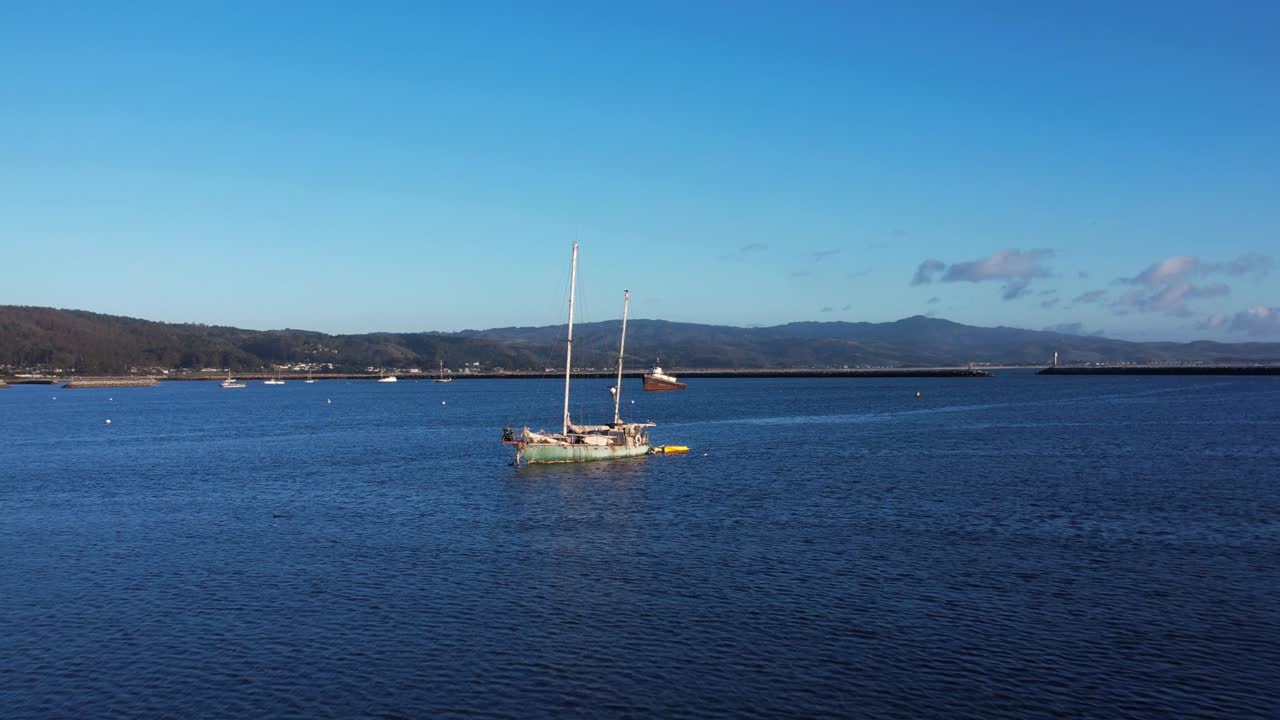 Drone push in towards anchored sailboat and tug boat in harbor at Mavericks Beach, California. Birds cross frame.  Slow motion: 59.94 FPS.