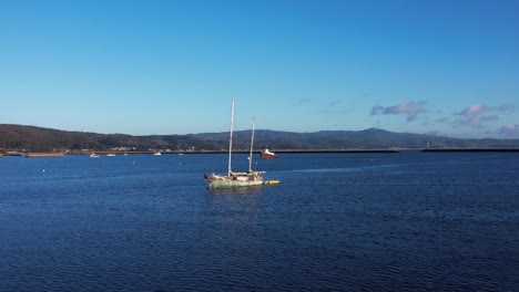 drone push in towards anchored sailboat and tug boat in harbor at mavericks beach, california. birds cross frame.  slow motion: 59.94 fps.
