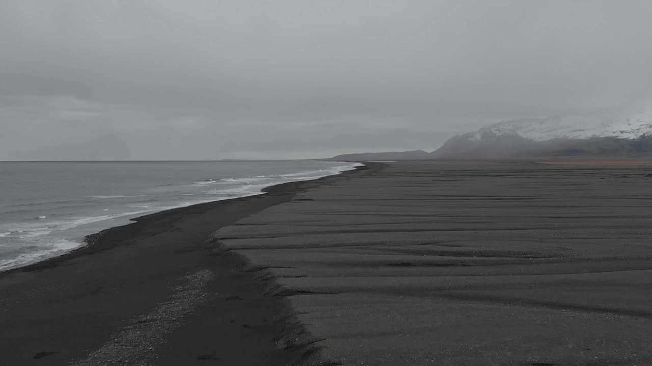 검은 모래 해변의 광활한 풍경을 따라 날아가는 설정 샷