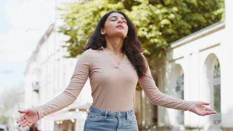 Indian-woman-taking-a-deep-breath-of-fresh-air,-relaxing,-taking-a-break-resting-meditating-outdoors