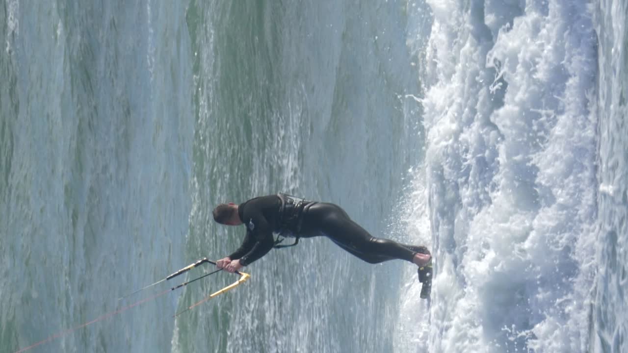 Close up tracking shot of kite surfer jumping and waving to camera. Vertical