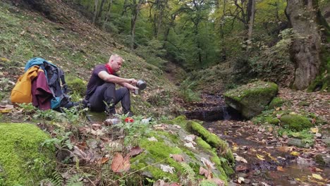 young man boils hot water for tea by green forest stream