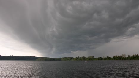 Grandes-Nubes-De-Tormenta-Ondeando-Y-Rodando-A-Través-Del-Marco-Mientras-Un-Solo-Remero-Atraviesa-Este-Lago-Urbano-Del-Medio-Oeste