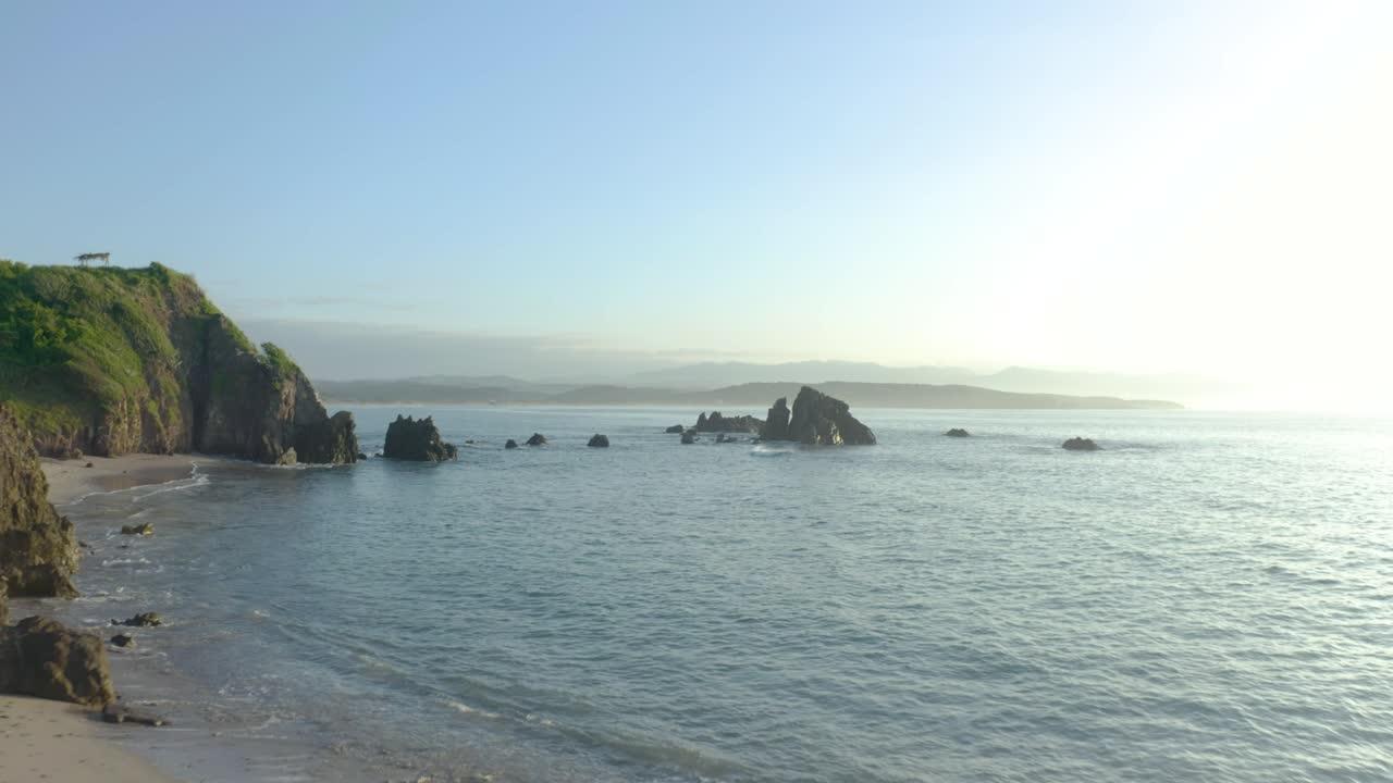 Aerial footage capturing a sunlit, dense green forest on a peninsula. The high-angle drone video showcases vibrant foliage, serene atmosphere, and expansive views under clear skies