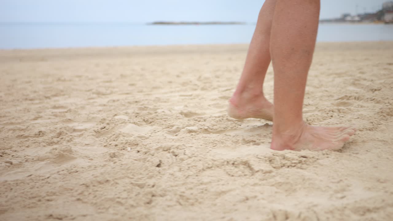 Tracking handheld shot of person&rsquo;s legs and barefeet walking across sandy beach