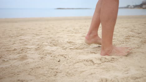 Tracking-handheld-shot-of-person’s-legs-and-barefeet-walking-across-sandy-beach