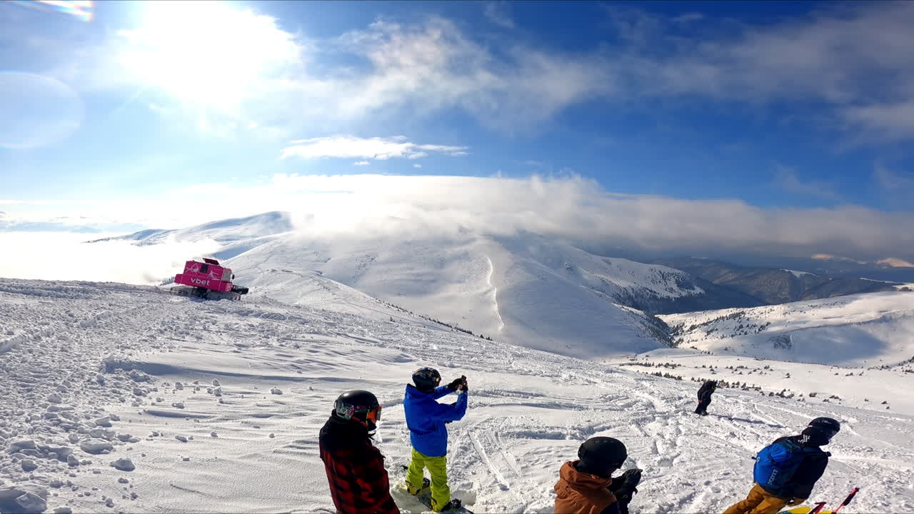 Group of people wearing helmets stand on the mountain top. Snowboarders and skiers are getting ready to go down the mount