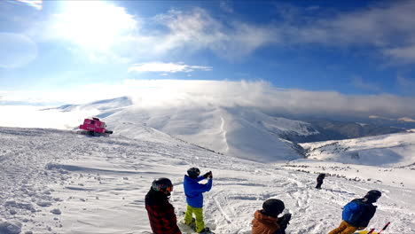 group of people wearing helmets stand on the mountain top. snowboarders and skiers are getting ready to go down the mount