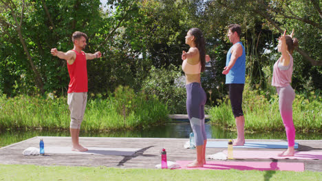 rear view of caucasian male instructor practicing yoga pose with diverse group in park