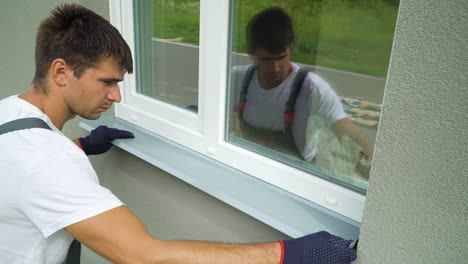 Man worker in protective gloves measuring external frame and PVC window metal sill size