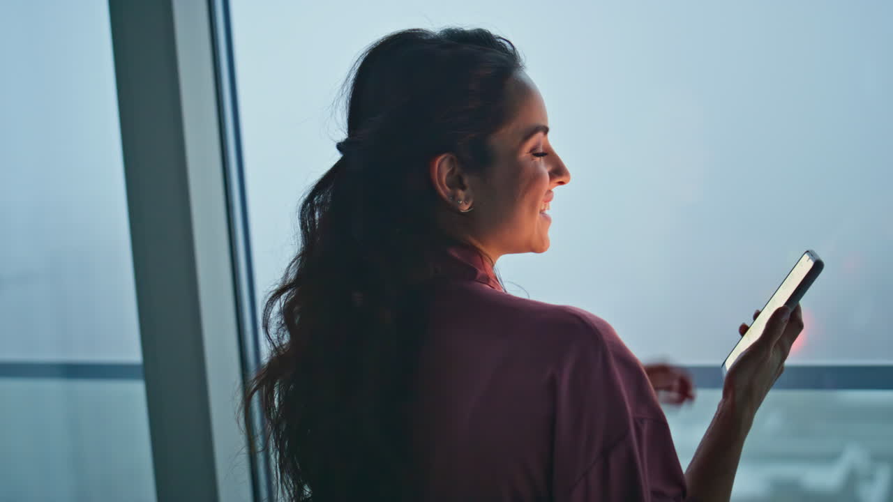 Brunette woman calling mobile phone at panoramic evening window flat back view