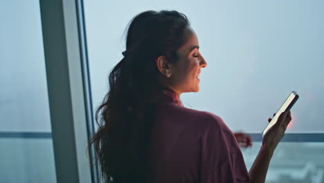 brunette woman calling mobile phone at panoramic evening window flat back view