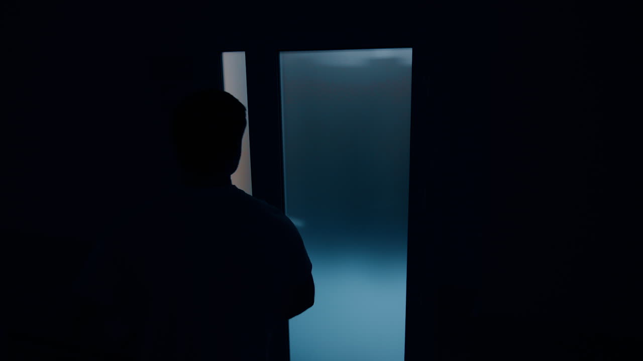 Dark male silhouette walking near the door in hospital. Husband is nervous for the wife giving birth to a baby.