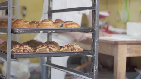 pastries cooling on baking sheets while a pastry chef rolls dough in the background