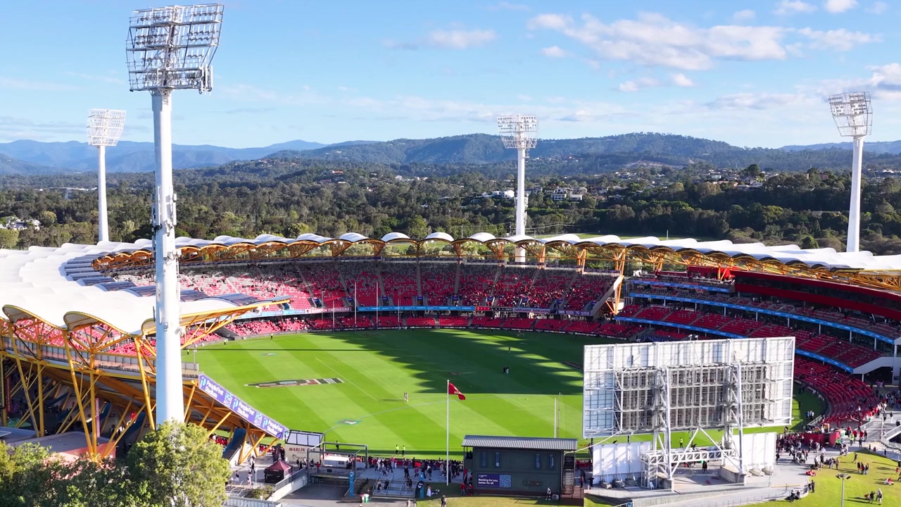 Wide aerial shot of a large sports arena with green field under bright daylight.