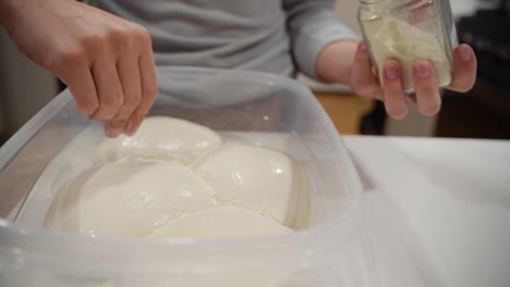 una persona poniendo harina sobre la masa de pizza cruda dentro de un recipiente, cierra la estática