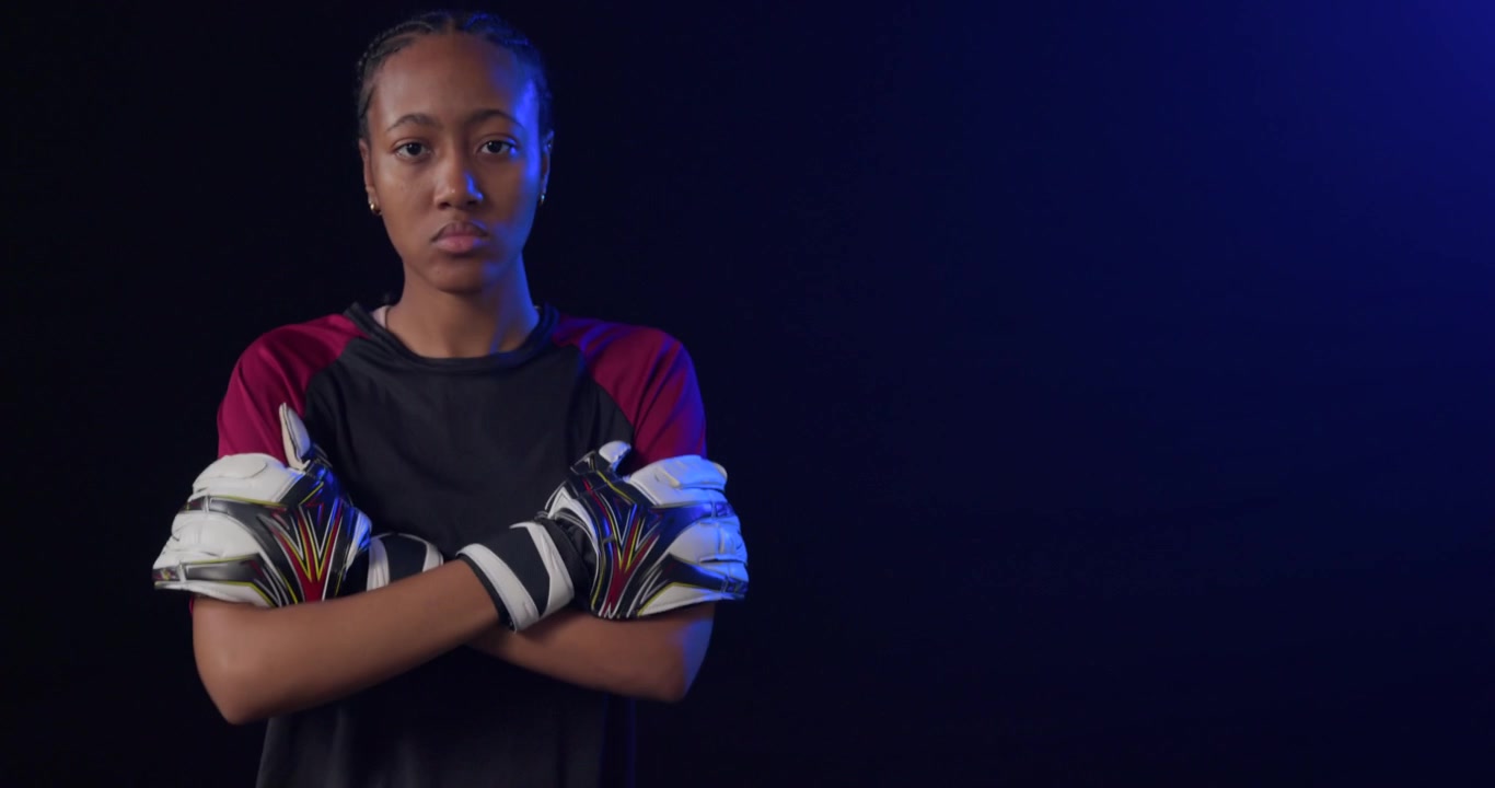 African American adult woman goalkeeper shifting ball, lifting knee, tapping ball, posing on turf