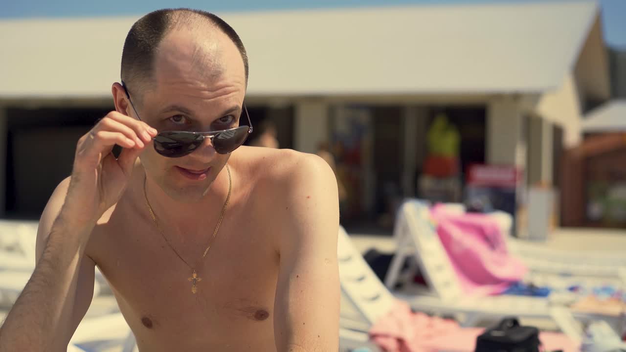 Close-up Italian man looks cunningly at girls He sits on the beach in lounger wearing sunglasses