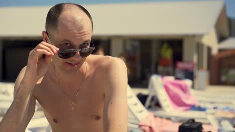 hombre italiano mira astutamente a las niñas se sienta en la playa en una tumbona con gafas de sol