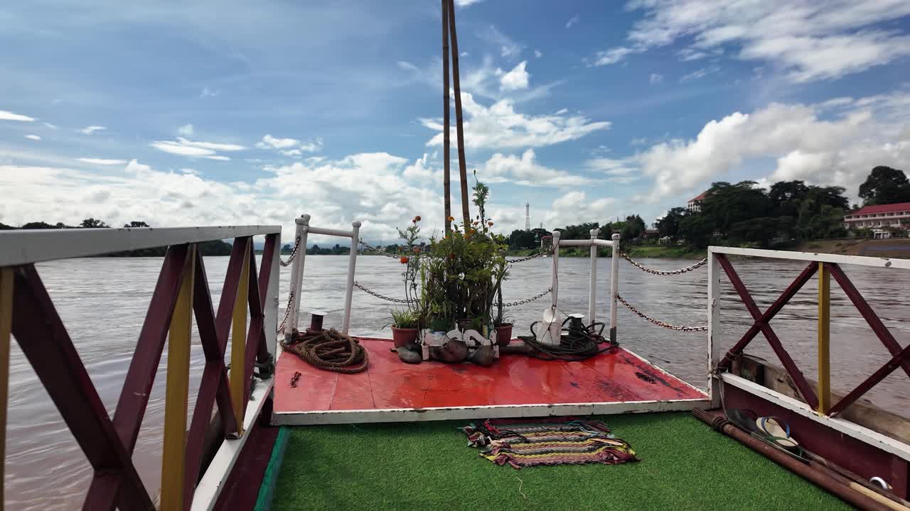 A vibrant Mekong river deck in Laos features plants, ropes, sandals, and a bright red platform