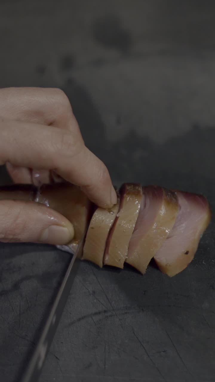 Hands slicing smoked or cured fish on a dark surface