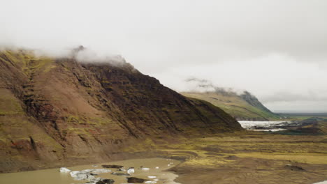 Pan-right-aerial-shot-of-Fjallsárlón-area-and-a-mountain-surrounded-by-clouds