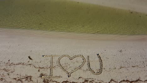 Ich-Liebe-Dich-In-Den-Sand-Geschrieben,-Während-Wasser-Auf-Den-Strand-Plätschert