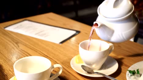 male hand pouring tea into white cup. cafe interior 4k