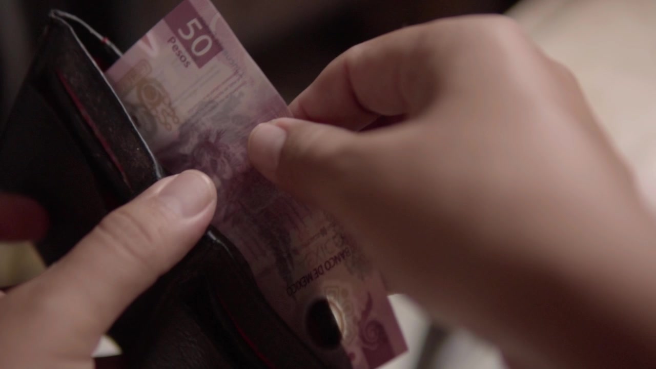 Detail osoby vyndávající bankovku z peněženky, zdůrazňující manipulaci s hotovostí, osobní finance, utrácení a každodenní správu peněz