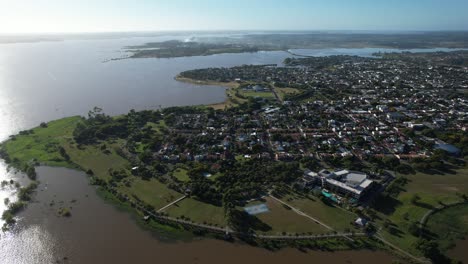 side tracking shot with drone showing the beautiful city of federacion, in argentina, the salto grande dam and many houses, harsh light and reflection of the sun in the water