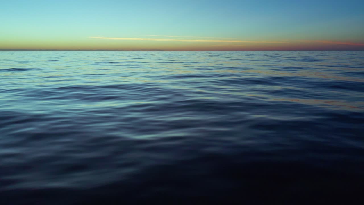 Calm ocean surface with small waves reflects fading sunlight during sunset, creating a peaceful and expansive seascape with a soft gradient sky above the horizon line