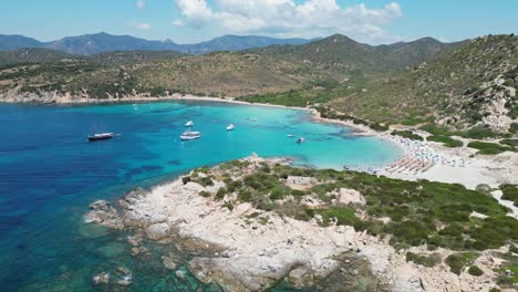 punta molentis beach in villasimius, sardinia - people and boats swim and relax in turquoise blue bay - aerial 4k