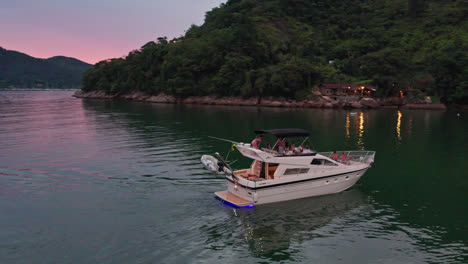 Yacht-in-Calm-sea-water-during-moody-sunset,-group-of-People-relaxing-on-board,-Aerial-drone-Orbiting