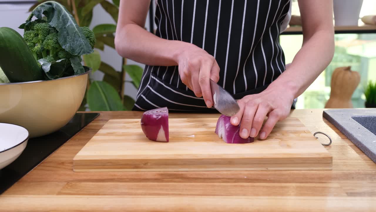 Giovane donna con grembiule a righe trita una cipolla rossa in cucina.