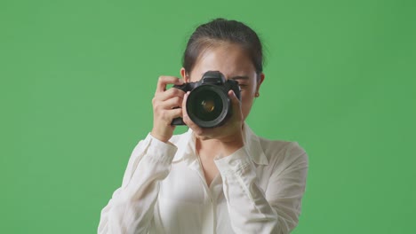 close up of asian photographer telling the model to move left and right while taking pictures by camera on green screen background in the studio