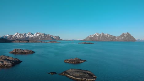 aerial drone shot of the blue ocean in lofoten, norway with rocks in the foreground and mountains in the background