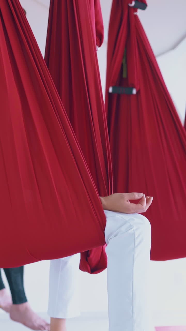 fingers in mudra position lie on women legs with bare feet sitting and meditating in special red hammocks close view