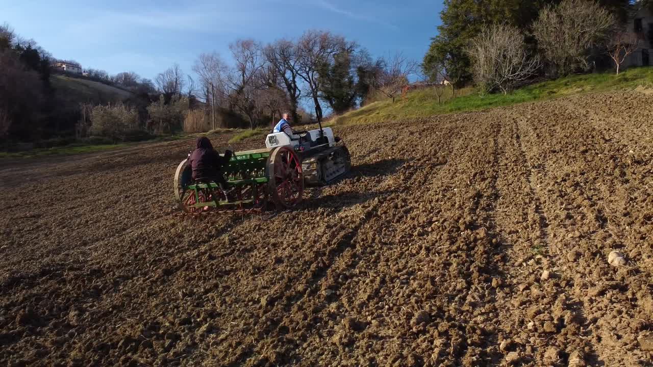 people on crawler tractor and seeder are sowing in the field at sunset, aerial approaching shot