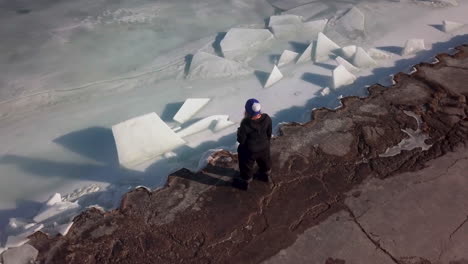 una mujer con un sombrero azul sostiene una bebida mientras está de pie al borde de un lago helado en canadá