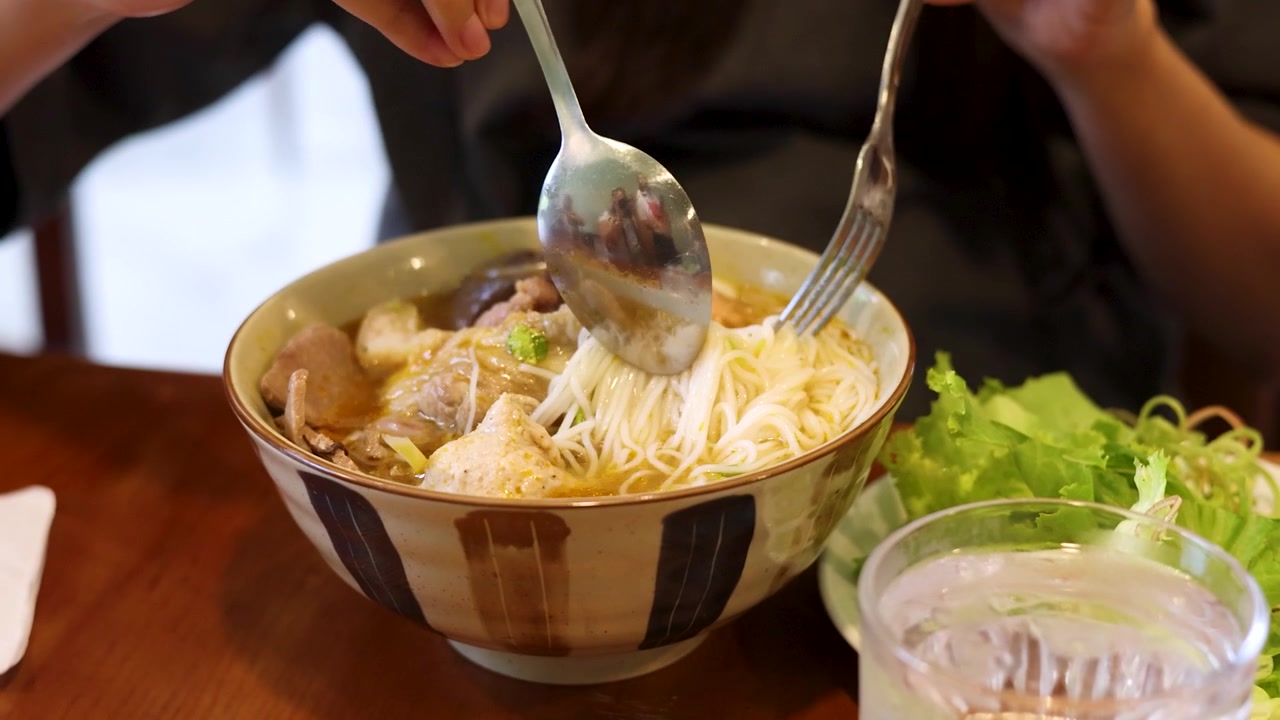 Cận cảnh đôi tay dùng thìa và dĩa để ăn phở Việt Nam.