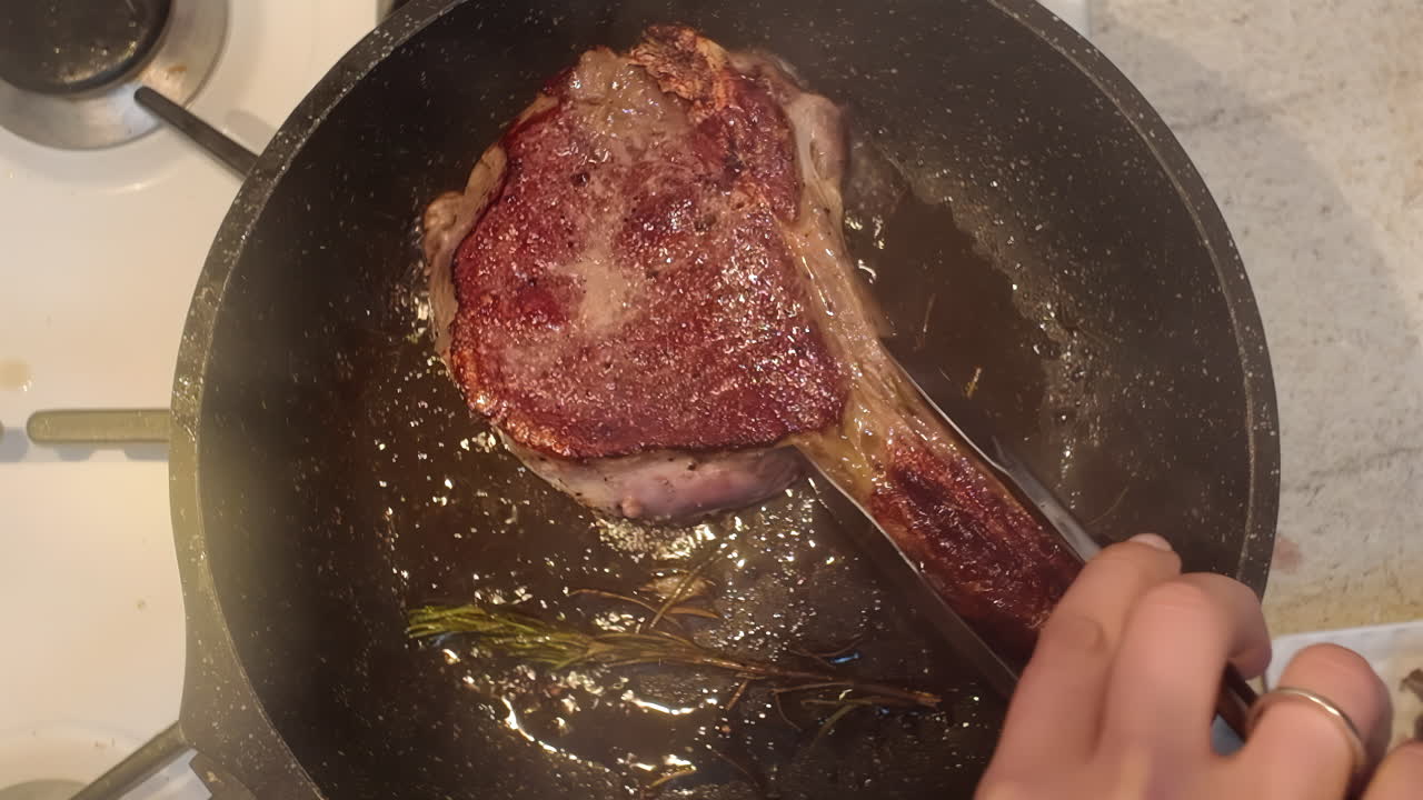 Cooking of a big red beef stake in a black pan with onion and rosemary