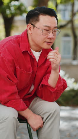 sad unhappy frustrated asian man sitting alone in city street, feeling bad, annoyed, grief, problem