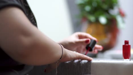 joven atractiva pintándose las uñas de color rojo en casa