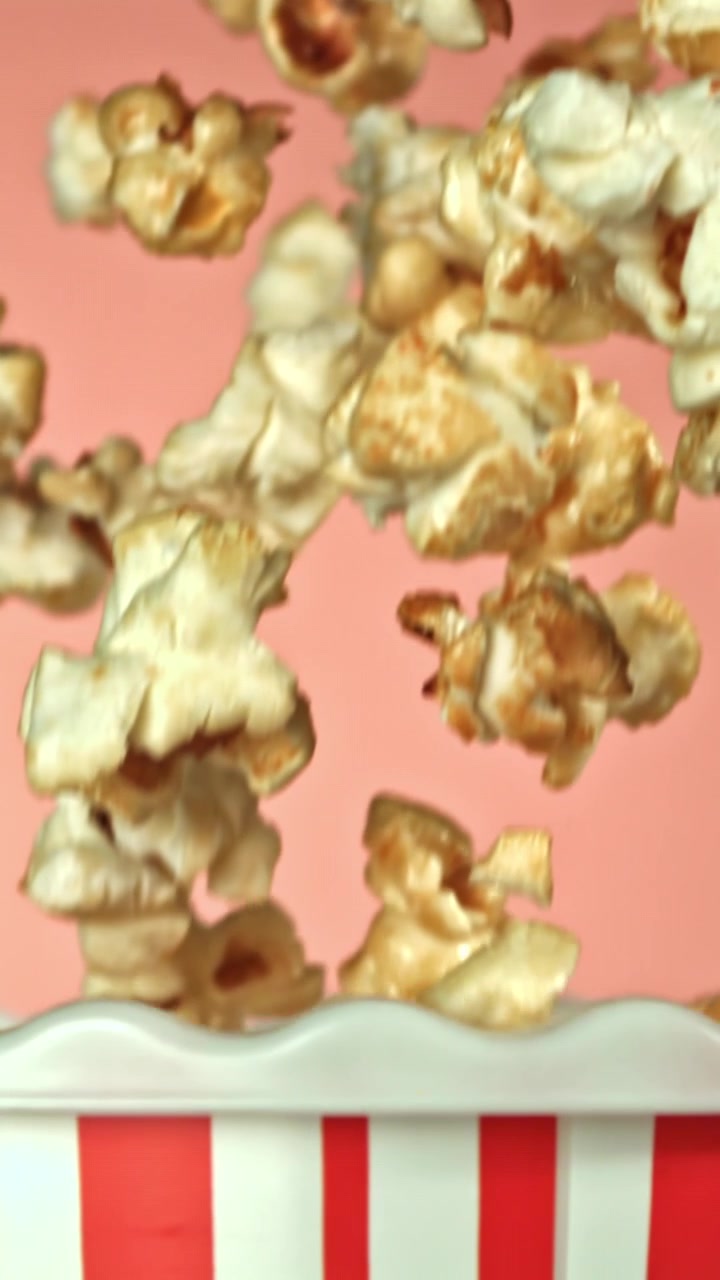 Popcorn che cadono in una scatola a righe su sfondo rosa