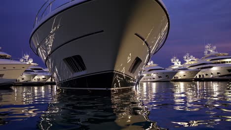 several large luxury yachts are moored in a tranquil marina at dusk, their lights reflecting on the calm water, creating a luxurious and peaceful atmosphere