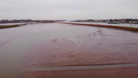 Aerial-Rising-Flying-Over-Flood-Plain-Beside-Noord-In-Ridderkerk-With-Ship-Passing-By-In-Distance